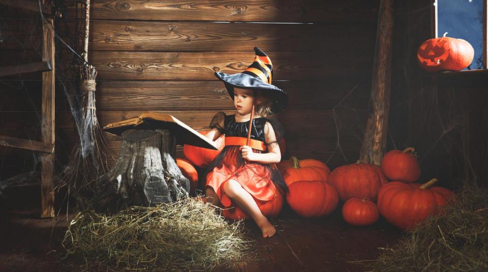 Little girl sitting among pumpkins with spell book
