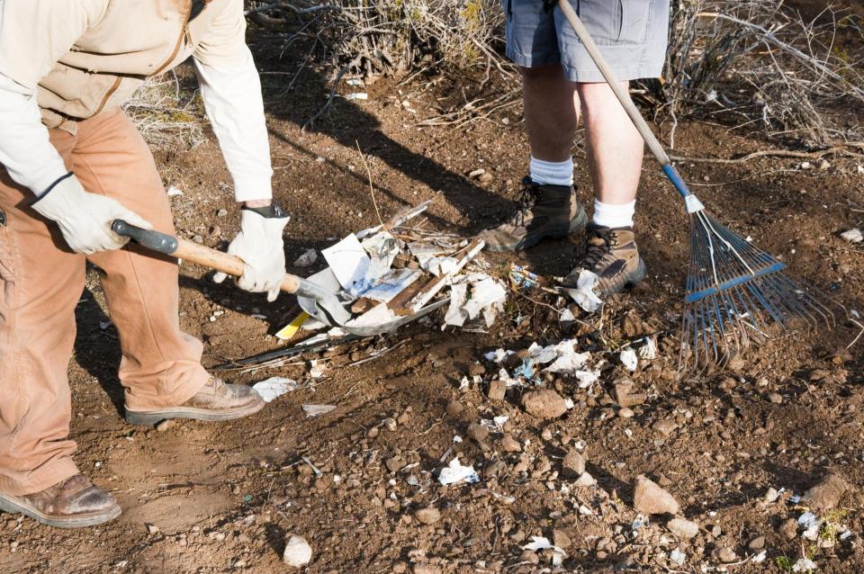 Lower portion of two people shoveling litter to clean up park