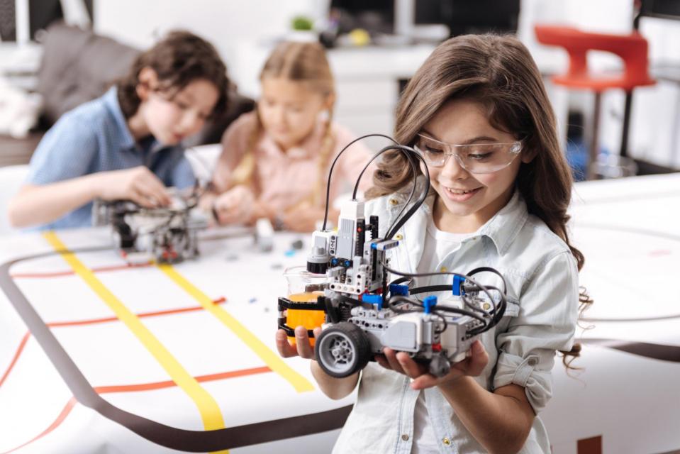Boys and girl in forefront with robot she built in her hands