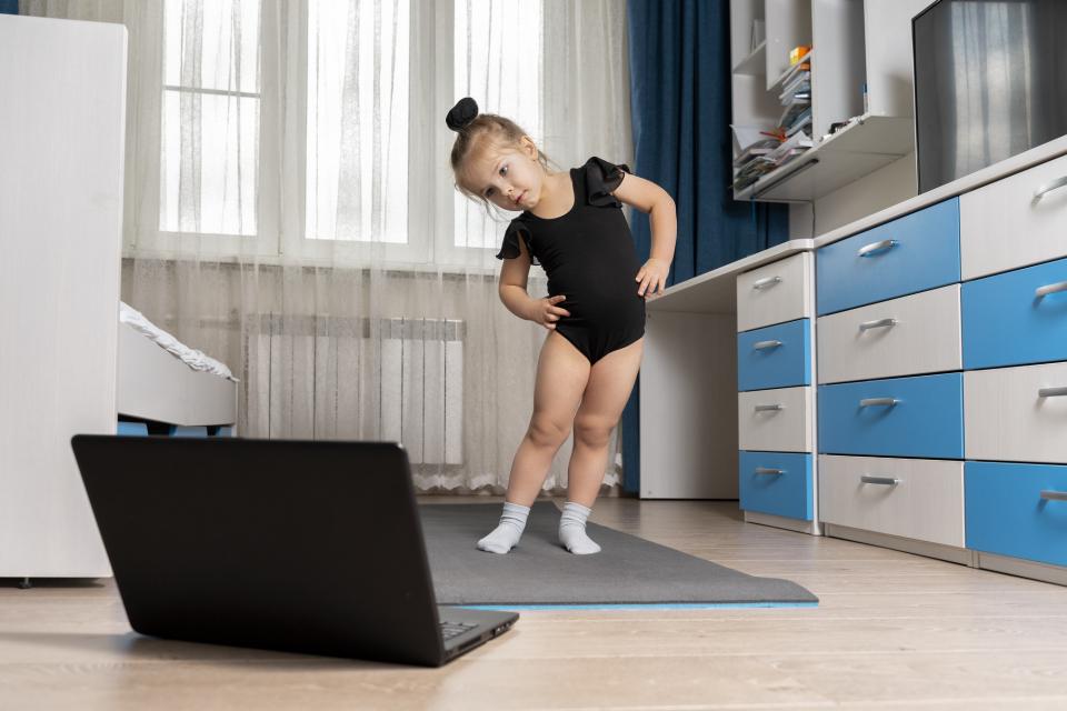 Little girl doing ballet in front of laptop computer