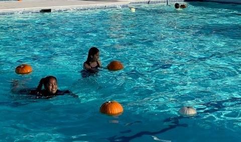 Pumpkins floating in a pool with swimmers