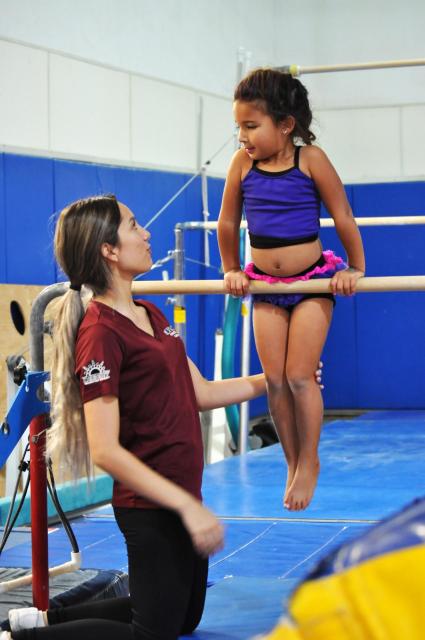 Gymnastics instructor trains student on the bars