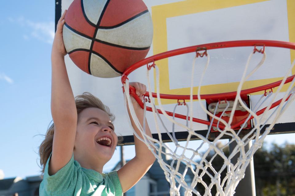 Young boy with big smile at top of rim of basketball net dunking a basketball